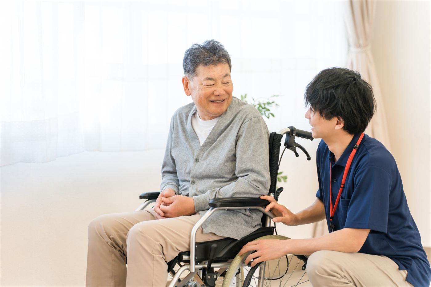 車椅子のシニア男性に寄り添って話を聞くスタッフ